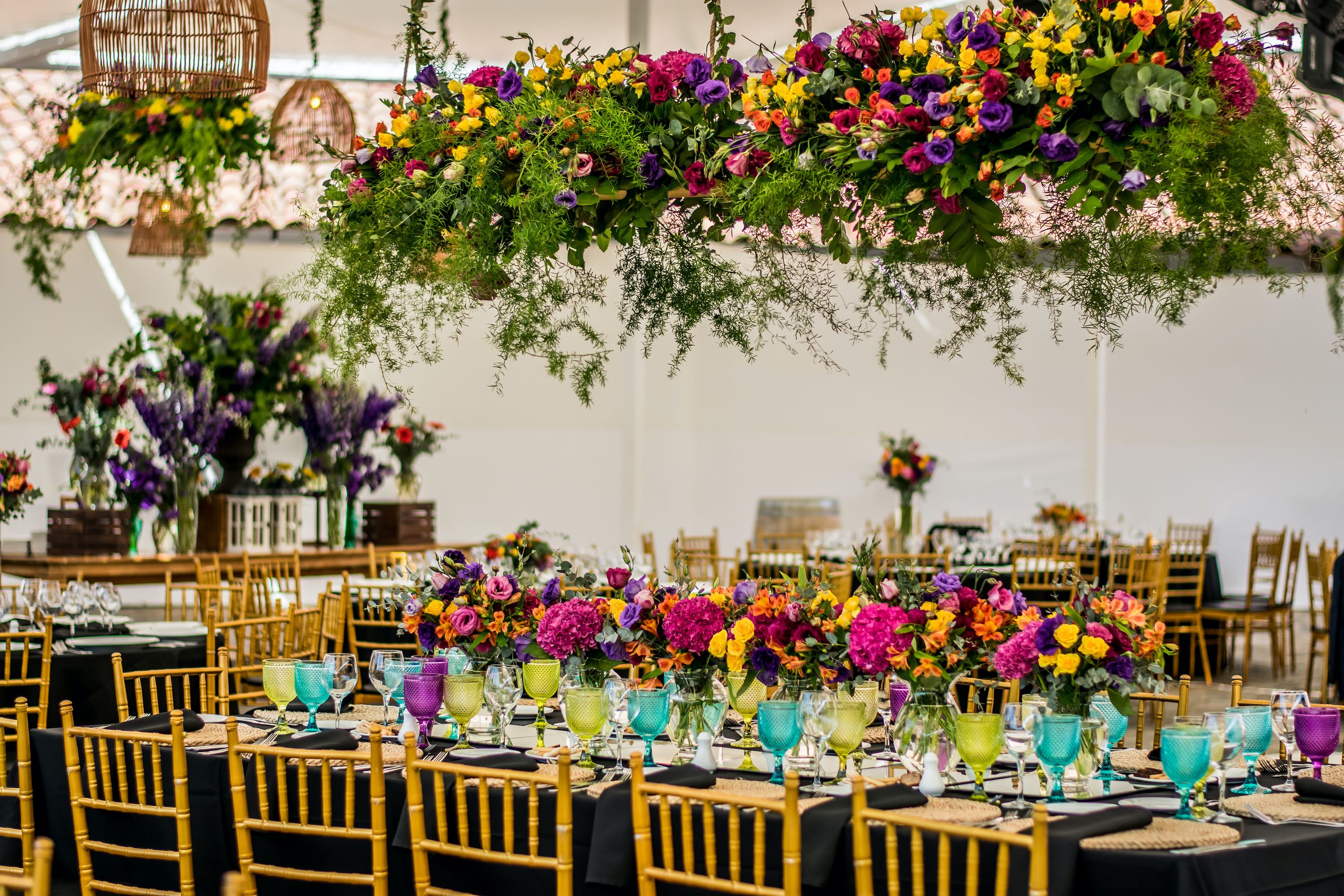 Mesa larga montada con copas de colores y centros florales vibrantes